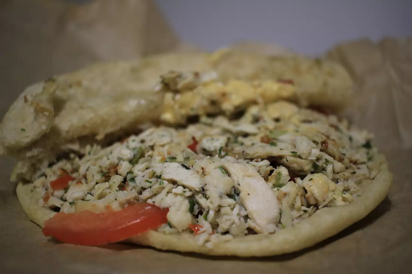 Bokit ouvert garni de poulet émincé, de tomate et d'herbes, posé sur du papier