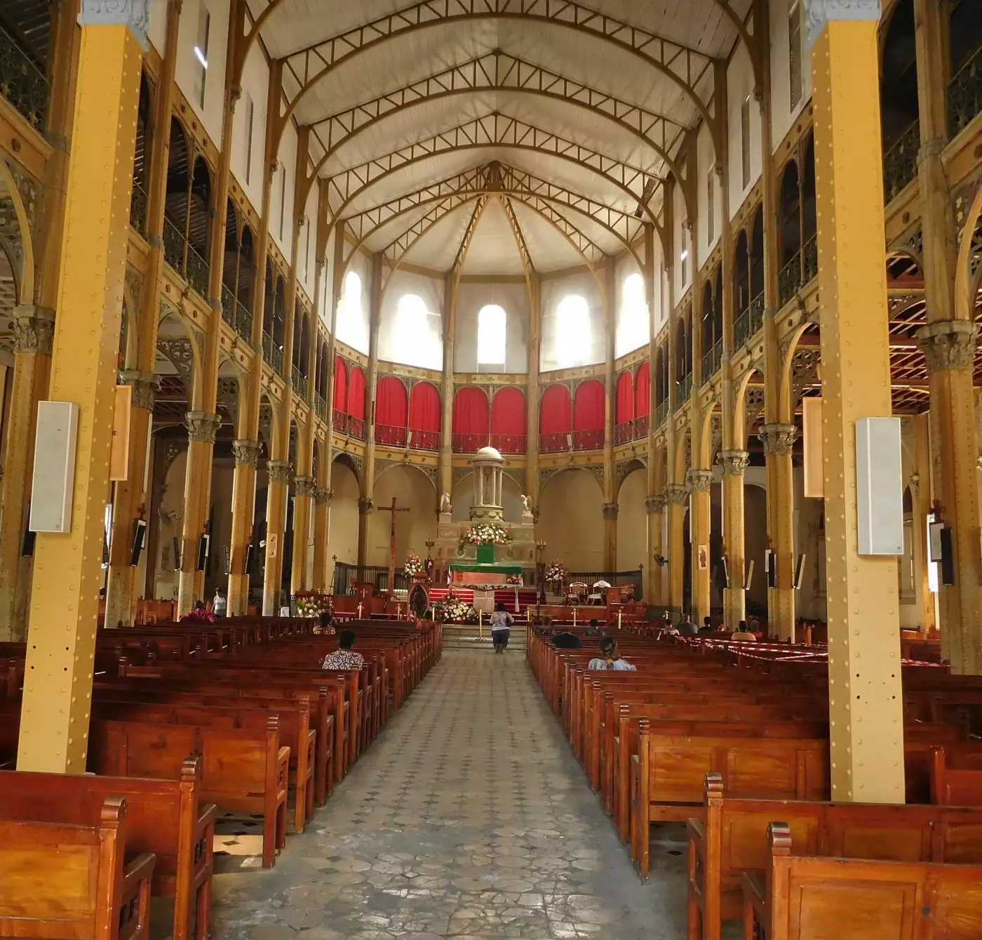 Intérieur de l'église Saint-Pierre-et-Saint-Paul de Pointe-à-Pitre, piliers et arcs métalliques rivetés peints en jaune au-dessus des bancs de bois