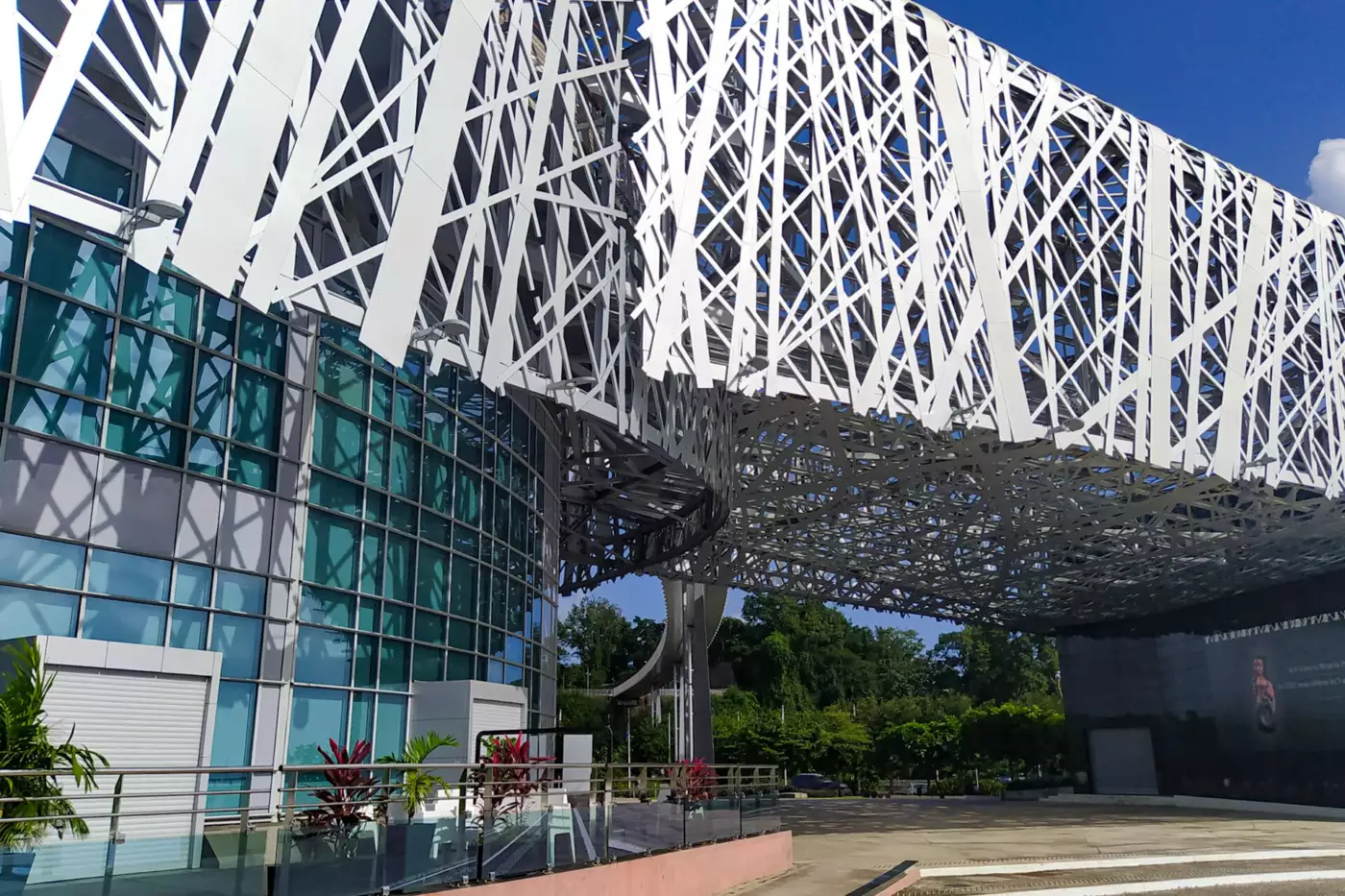 Façade vitrée du Mémorial ACTe surmontée de son entrelacs d'acier blanc, avec la passerelle qui monte vers le Morne Mémoire