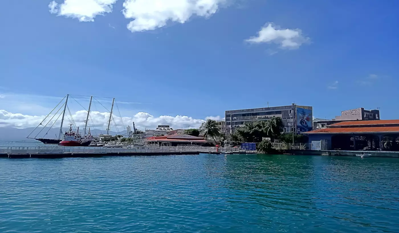La darse de Pointe-à-Pitre vue depuis l'eau, remorqueurs à quai, pontons et reliefs de Basse-Terre à l'horizon