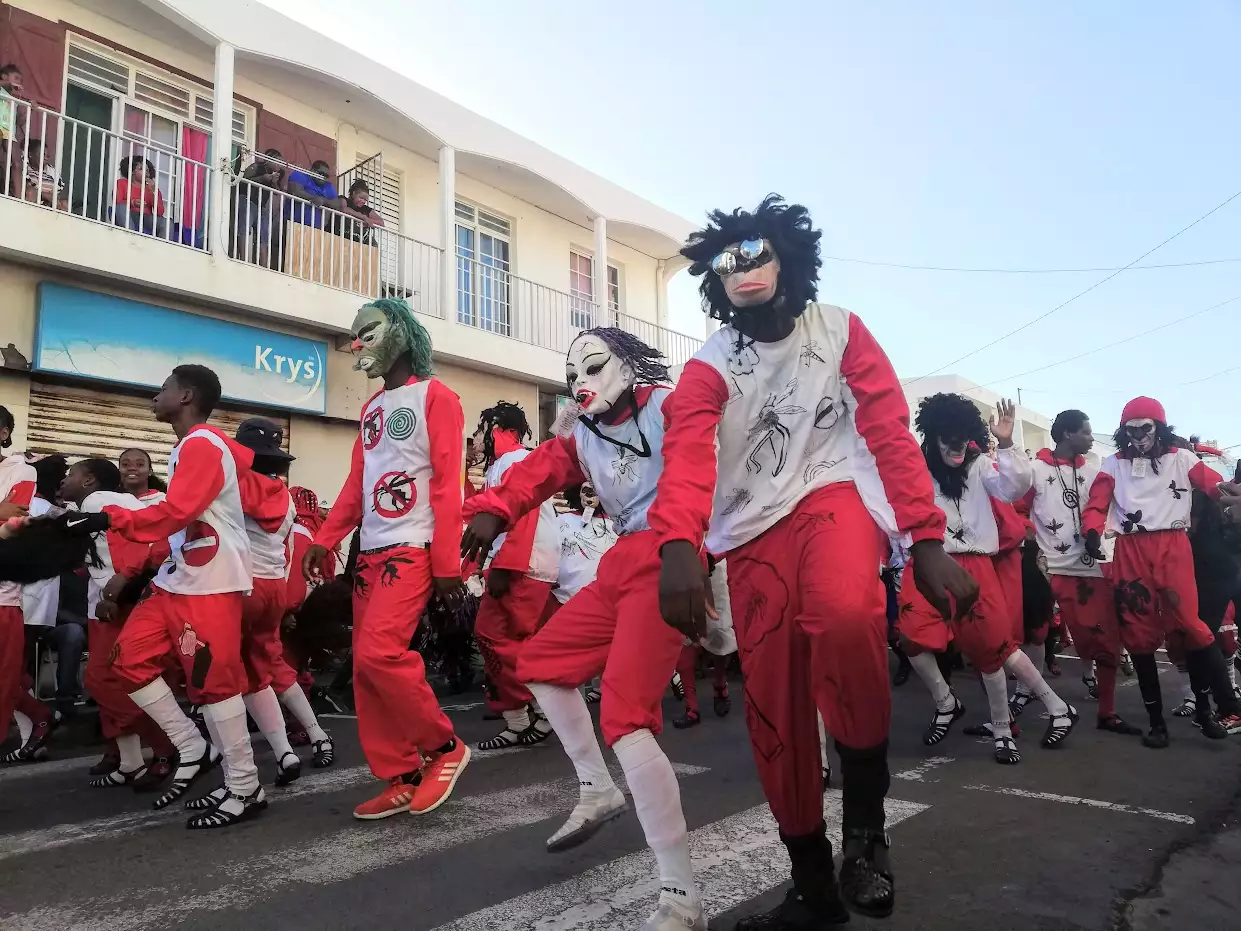 Danseurs masqués en tenue rouge et blanche défilant dans une rue du Moule pendant le carnaval
