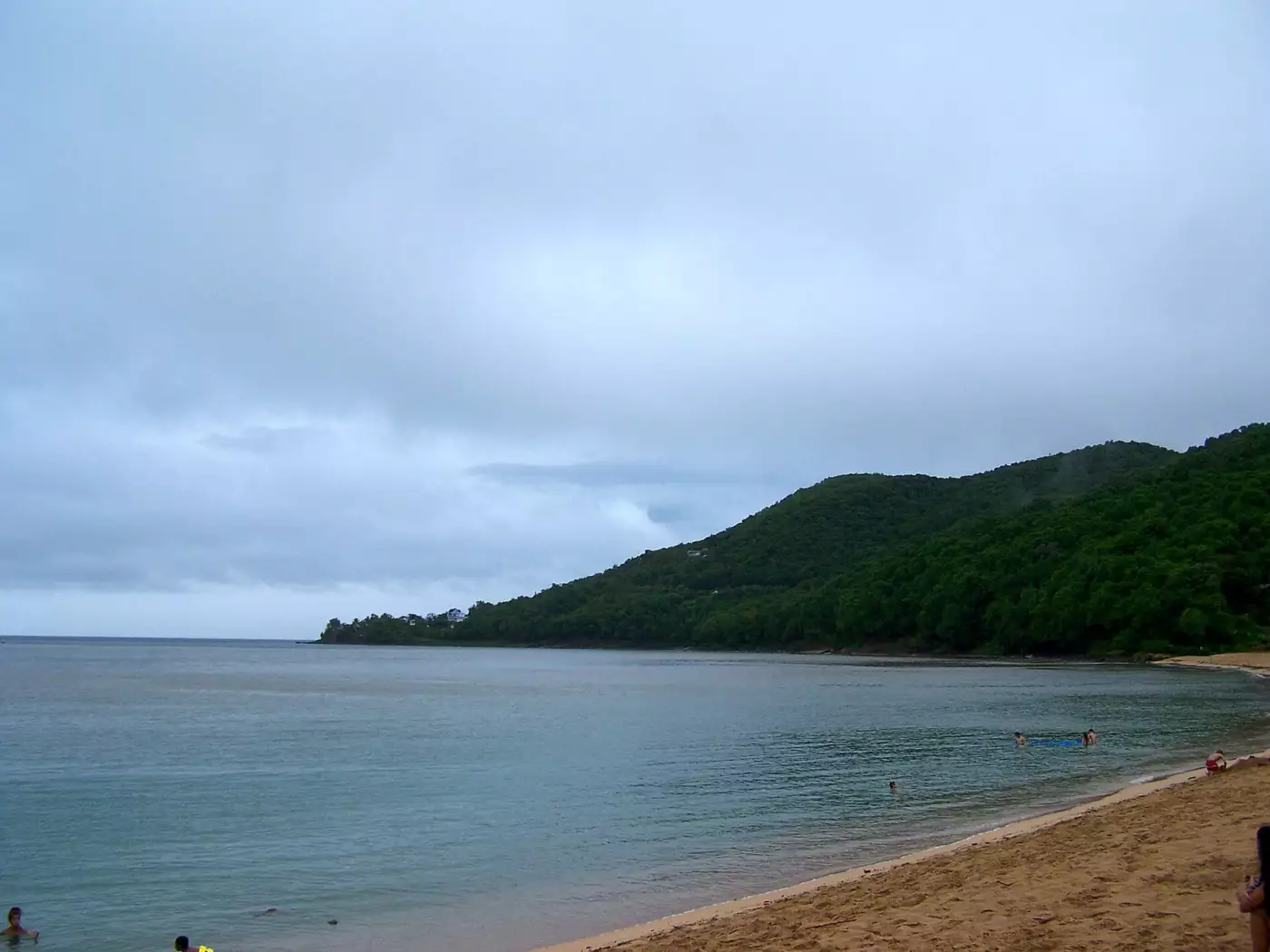 Courbe de sable doré et morne boisé au nord de la plage de Grande Anse, à Deshaies, sous un ciel couvert