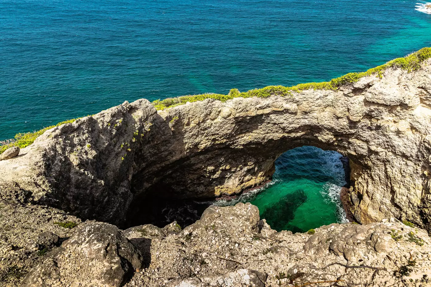 Arche calcaire effondrée au bord de la mer, eau turquoise au fond du gouffre