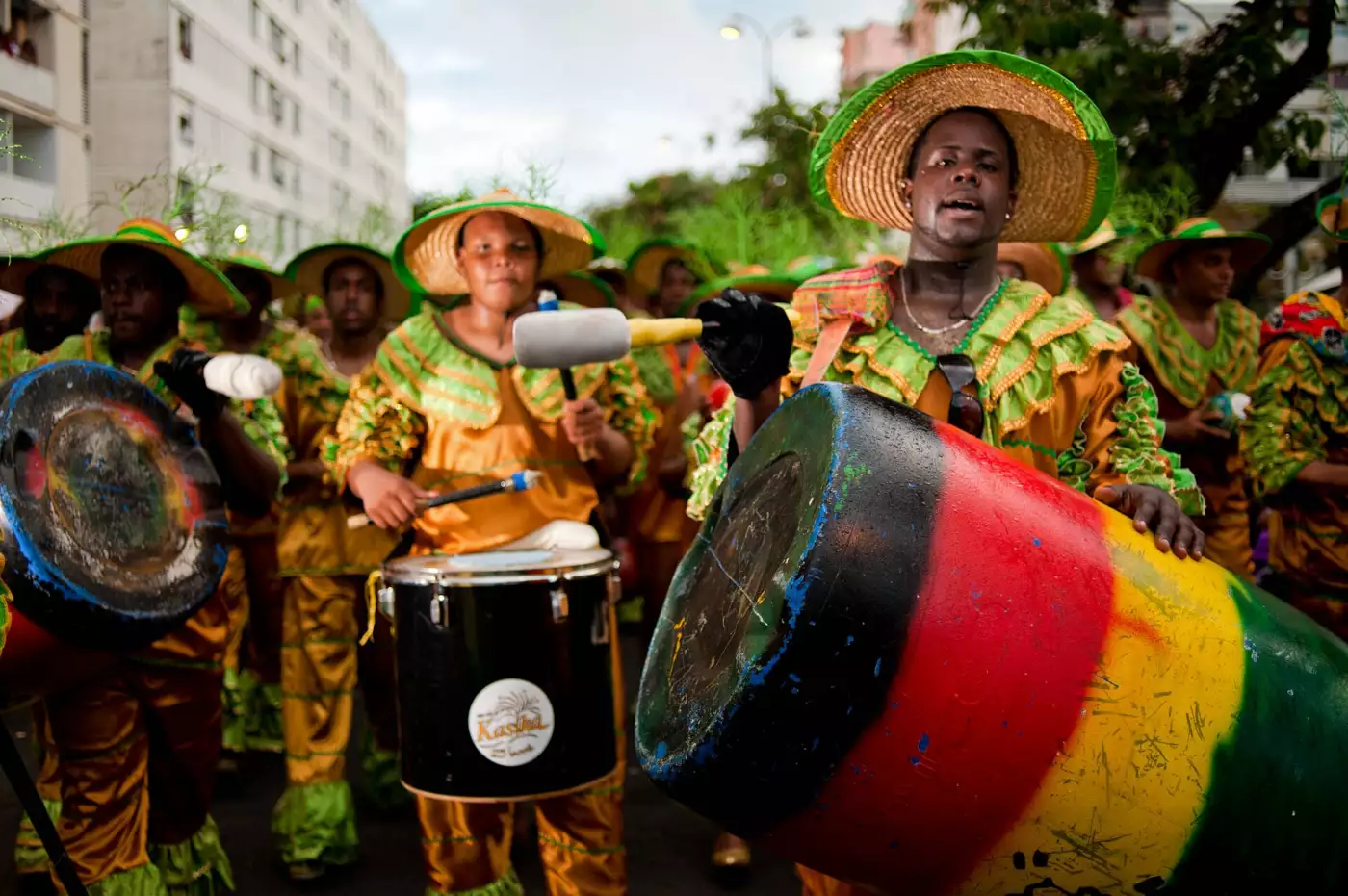 Percussionnistes en costume orange et vert portant tambours et caisse claire dans une rue de Pointe-à-Pitre pendant le carnaval