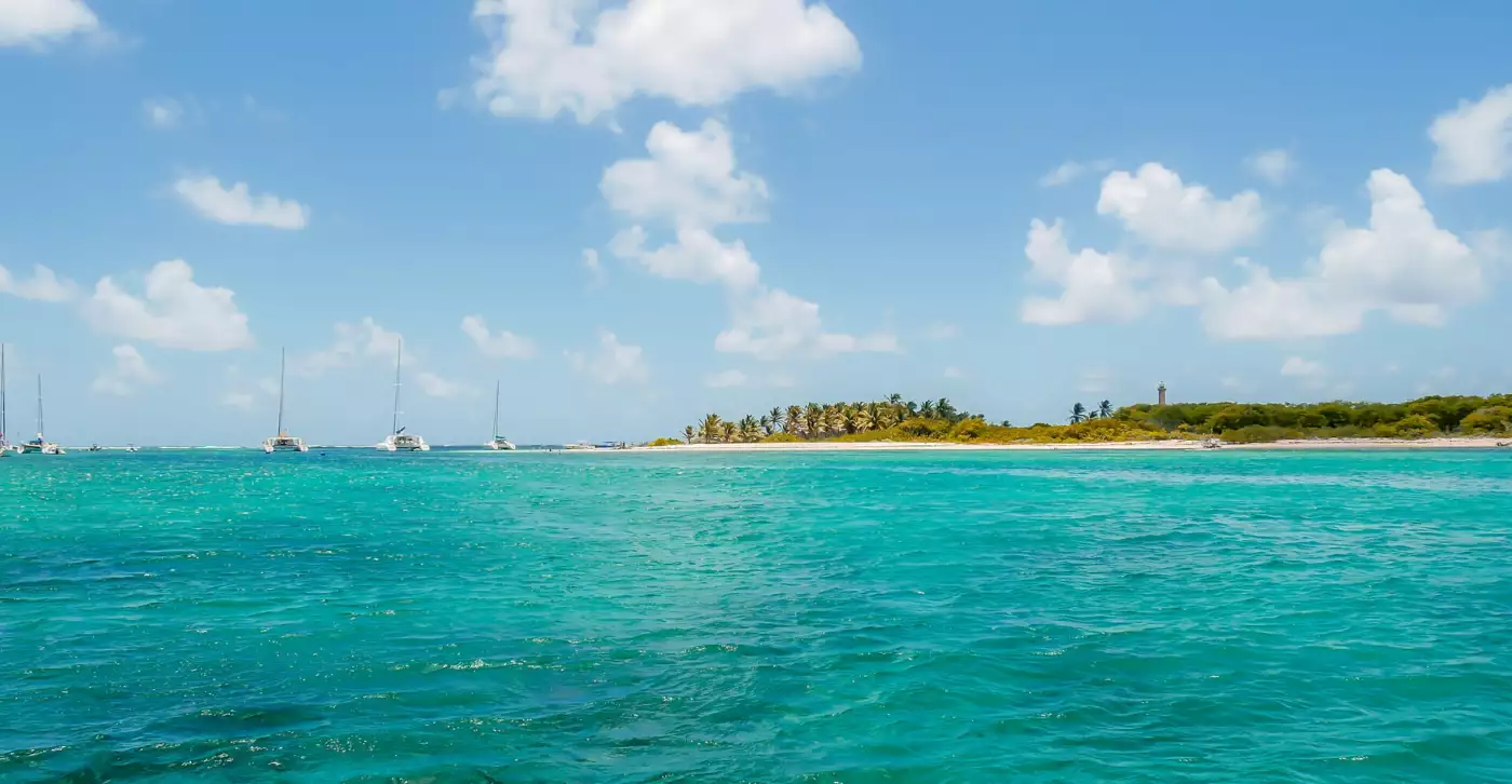 Arrivée dans le lagon de Petite-Terre, catamarans au mouillage devant la plage et le phare à l'horizon