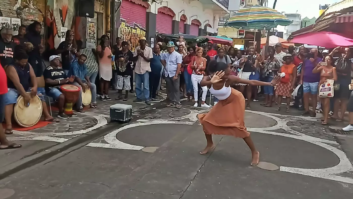 Danseuse de gwo ka au centre d'un cercle, face à trois joueurs de tambour ka assis, dans une rue de Pointe-à-Pitre