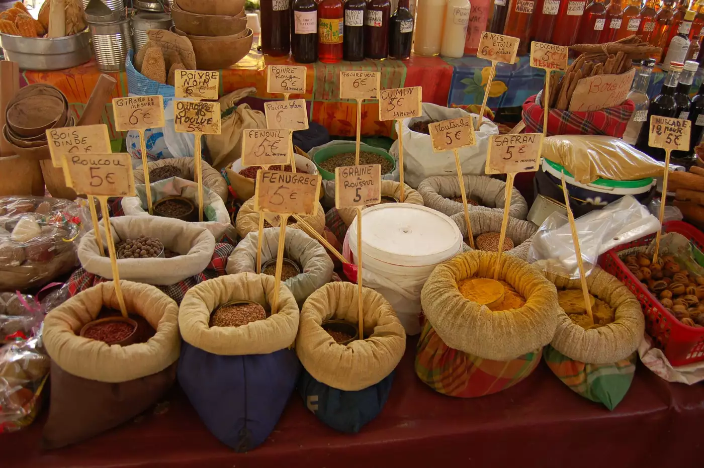 Étal d'épices en sacs sur un marché de Pointe-à-Pitre, avec pancartes indiquant bois d'Inde, roucou, colombo, fenugrec et muscade