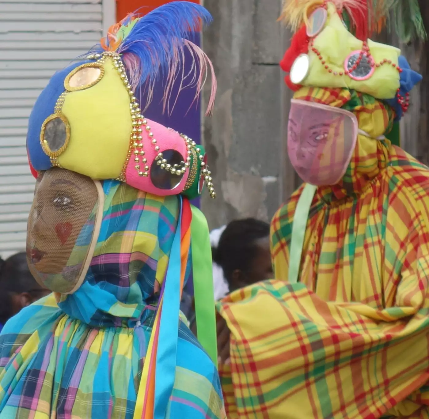 Deux carnavaliers masqués en robe de madras, coiffes garnies de miroirs et de plumes, au carnaval de Basse-Terre