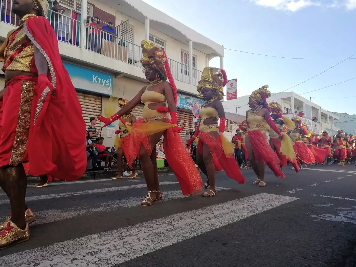 Danseuses en costume rouge et or d'un groupe à caisse claire défilant dans une rue du Moule