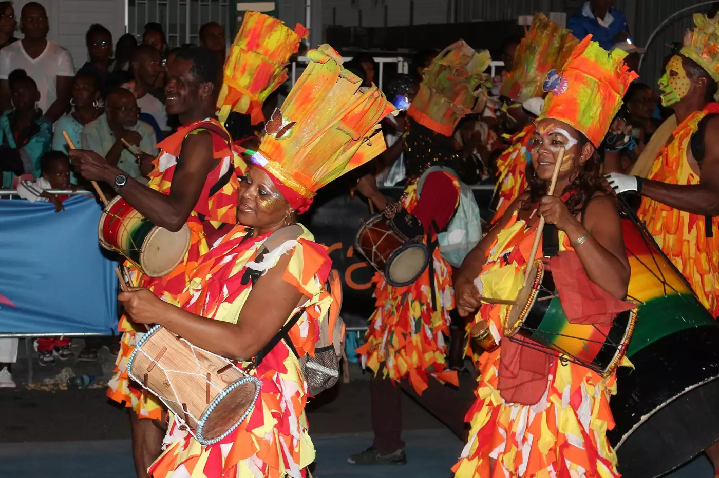 Percussionnistes en costume orange et jaune avec tambours et hautes coiffes lors d'un défilé nocturne à Saint-François