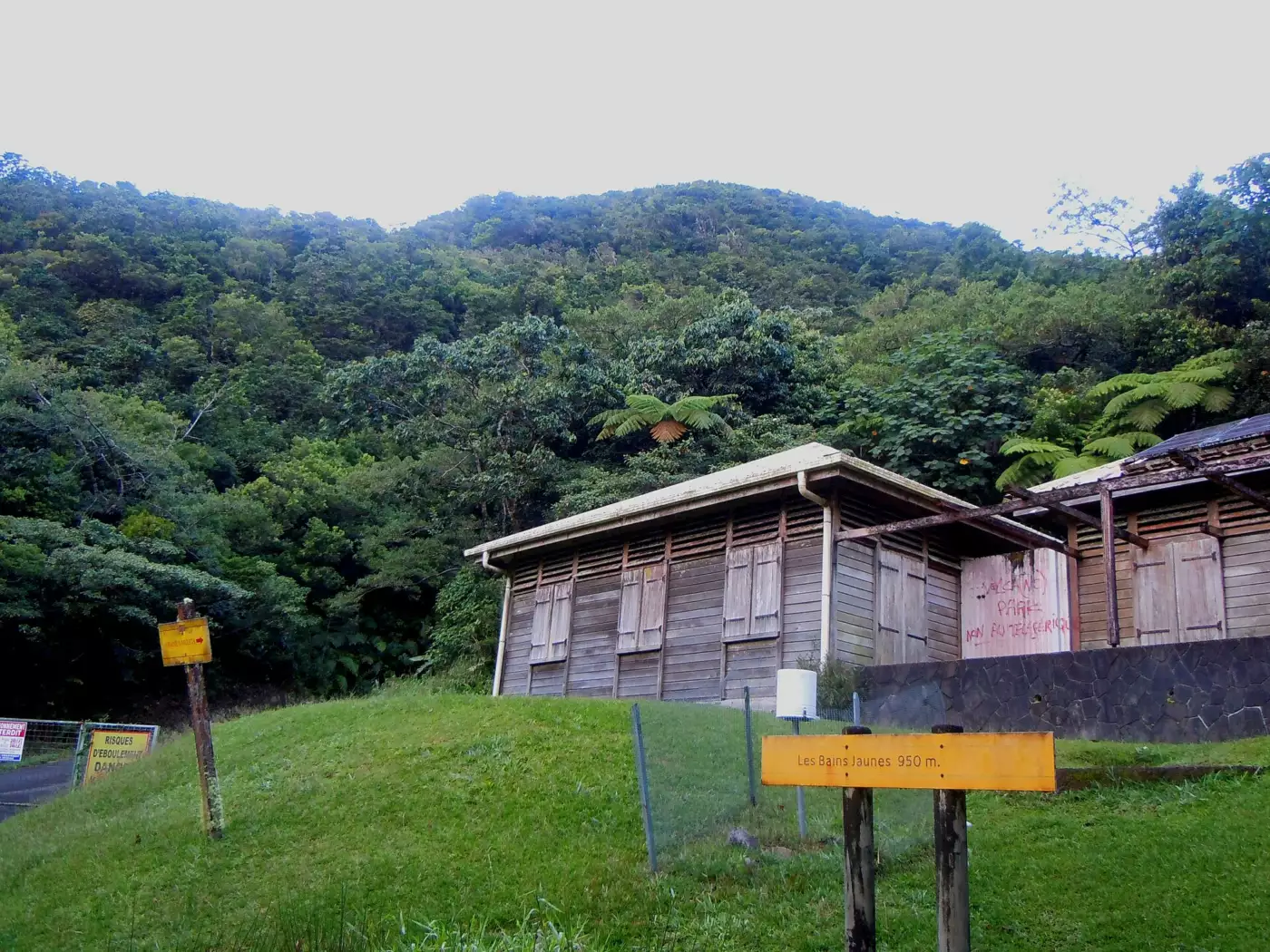 Le site des Bains Jaunes en lisière de forêt, son panneau d'altitude 950 m et l'ancienne Maison du Volcan aux volets fermés