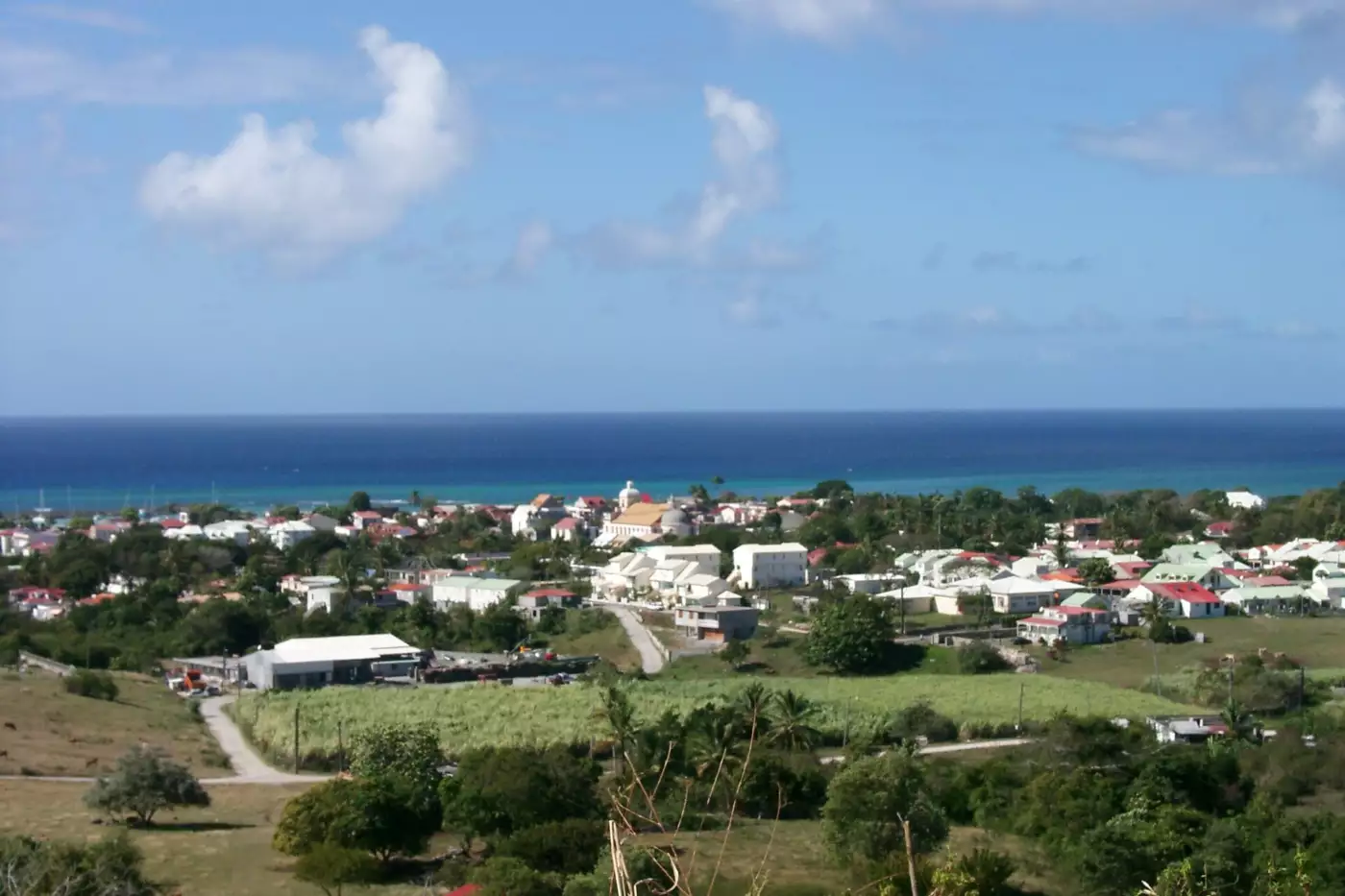 Grand-Bourg vu des hauteurs, toits rouges et clocher au-dessus d'un champ de canne, la mer à l'horizon