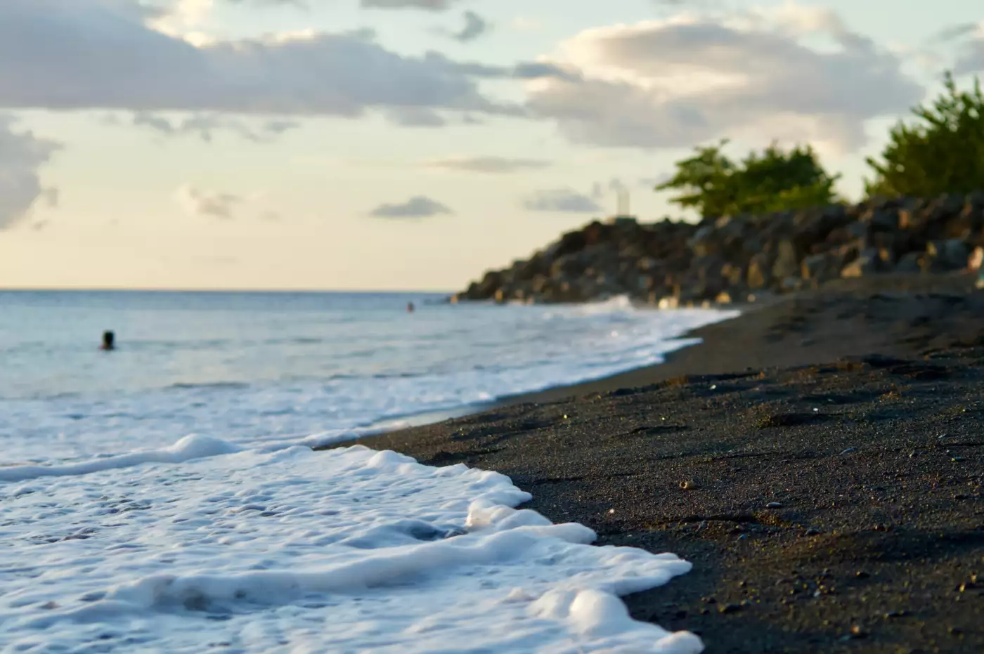 Vagues calmes sur une plage de sable noir de Guadeloupe au coucher du soleil