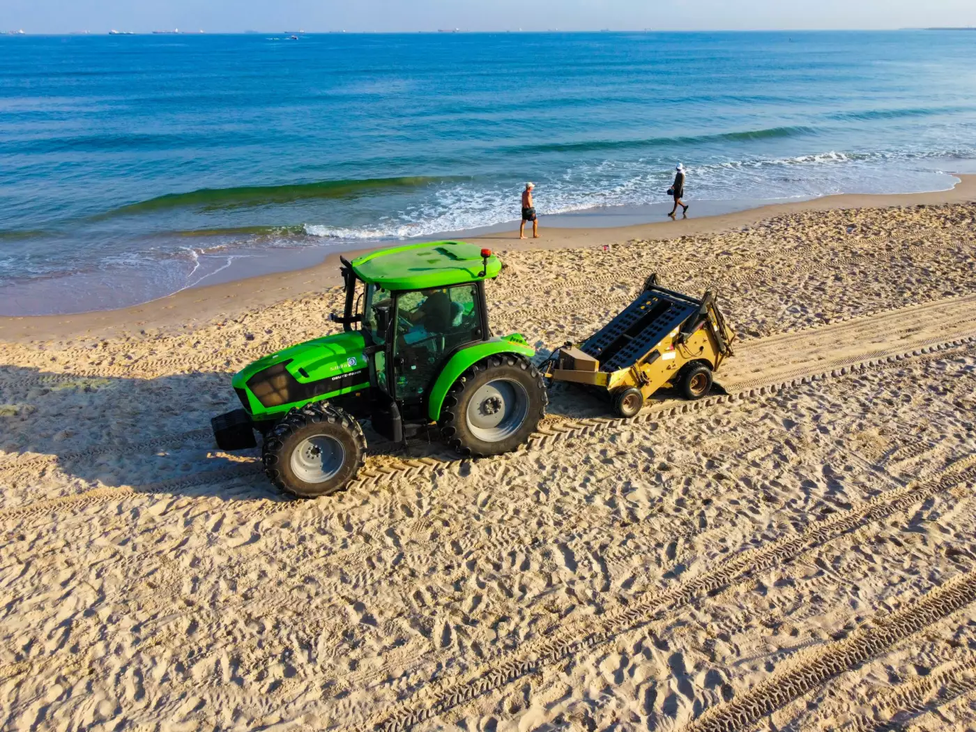 Tracteur tractant un râteau ramasseur sur le haut d'une plage de sable, opération de nettoyage mécanisé