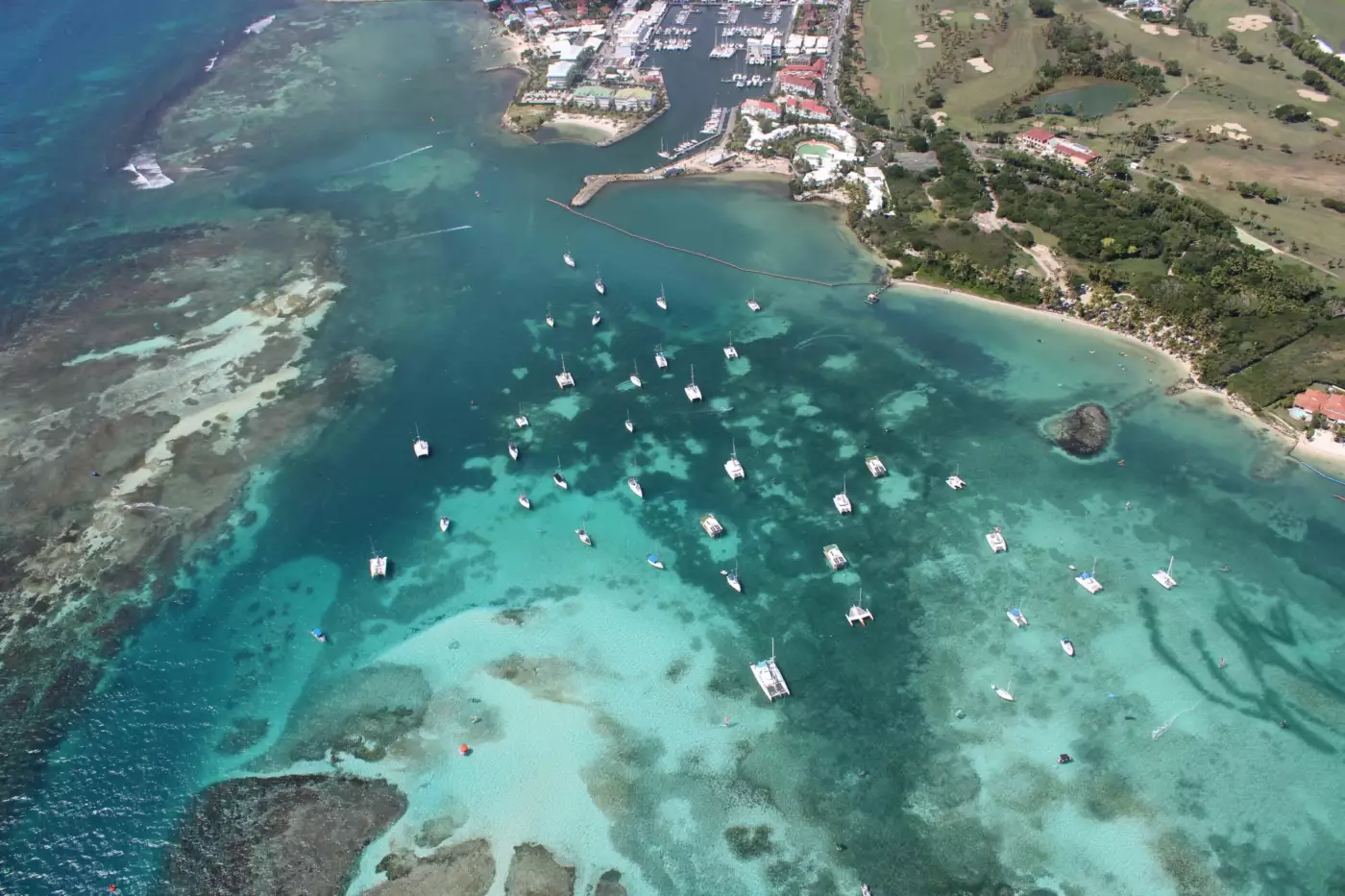 Vue aérienne d'un lagon turquoise avec des voiliers au mouillage et une côte verdoyante