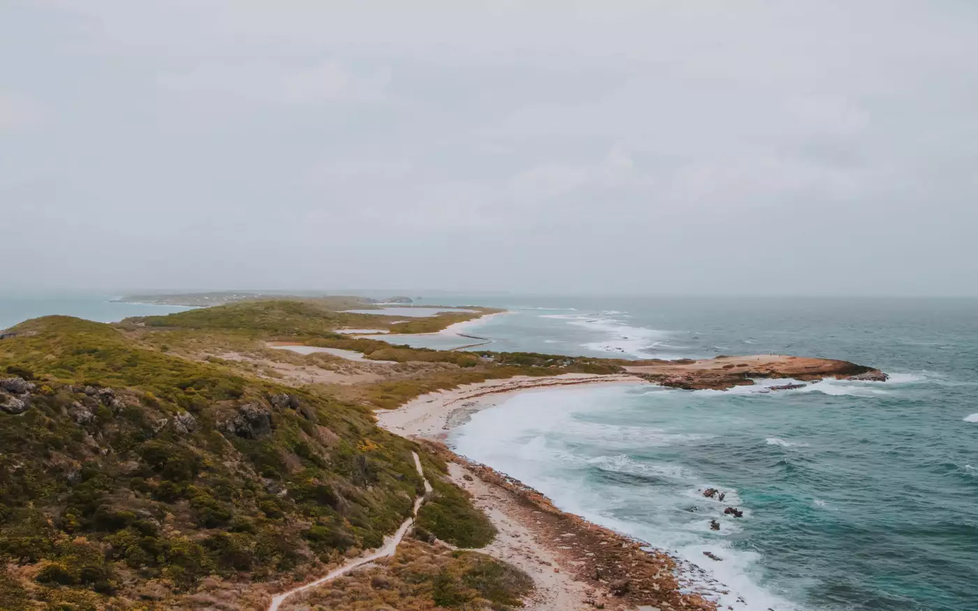 Côte rocheuse couverte de végétation sèche dominant une mer écumante