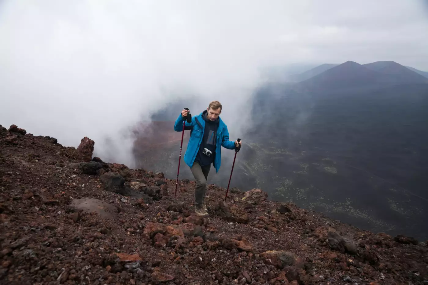 Randonneur avec des bâtons progressant dans la brume sur un paysage volcanique dénudé